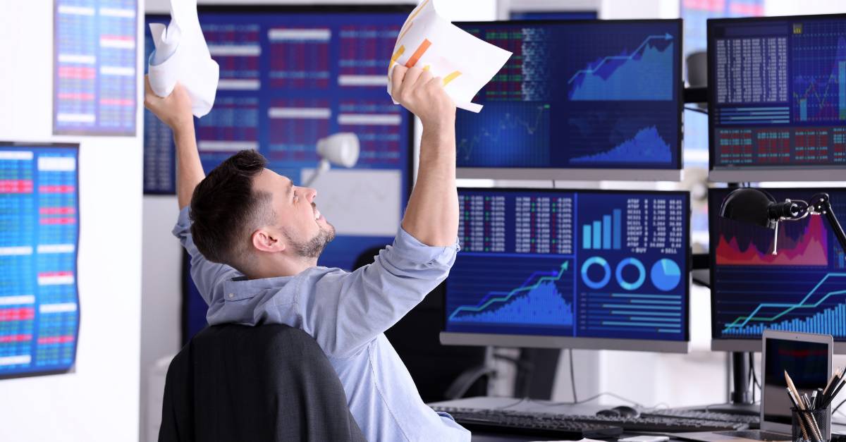 man rejoicing in front of trading monitors